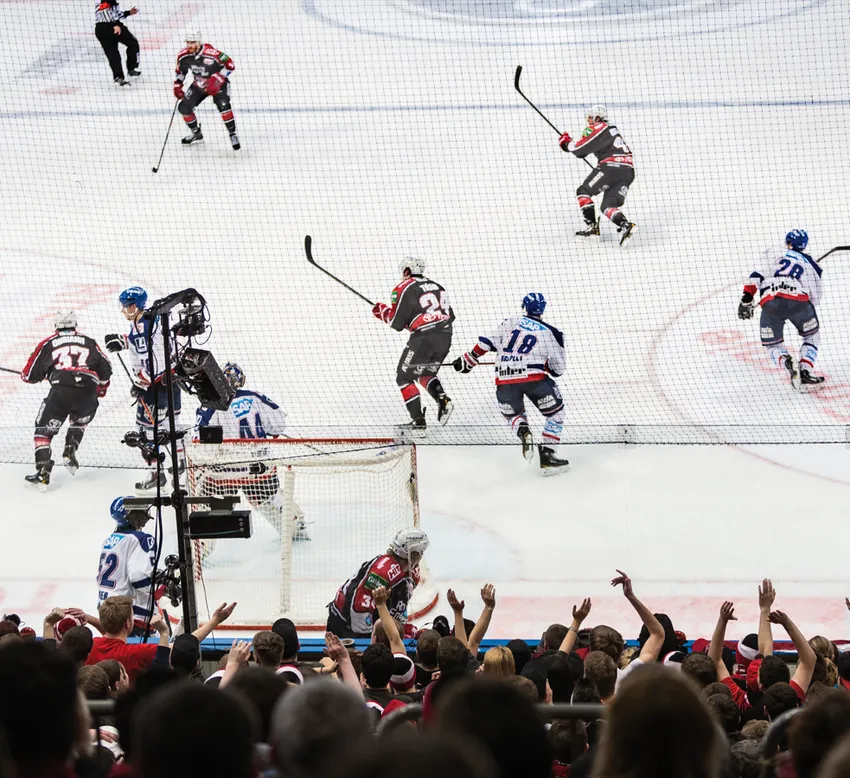 Een dynamische ijshockeyscene met spelers in actie op het ijs en een juichende menigte op de achtergrond.