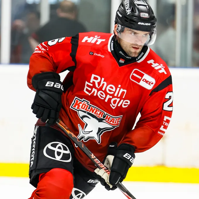 Een ijshockeyspeler in een rood shirt met het logo van Rhein Energie en Kölner Haie, op het ijs.