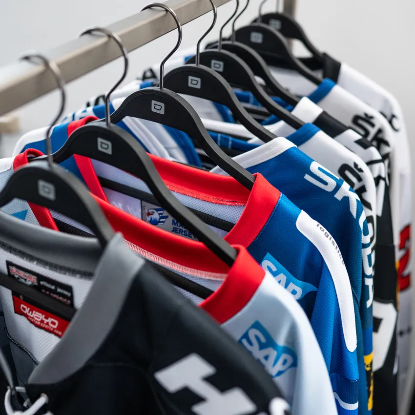 Zeven kleurrijke ijshockeyshirts hangen aan een kledingrek.