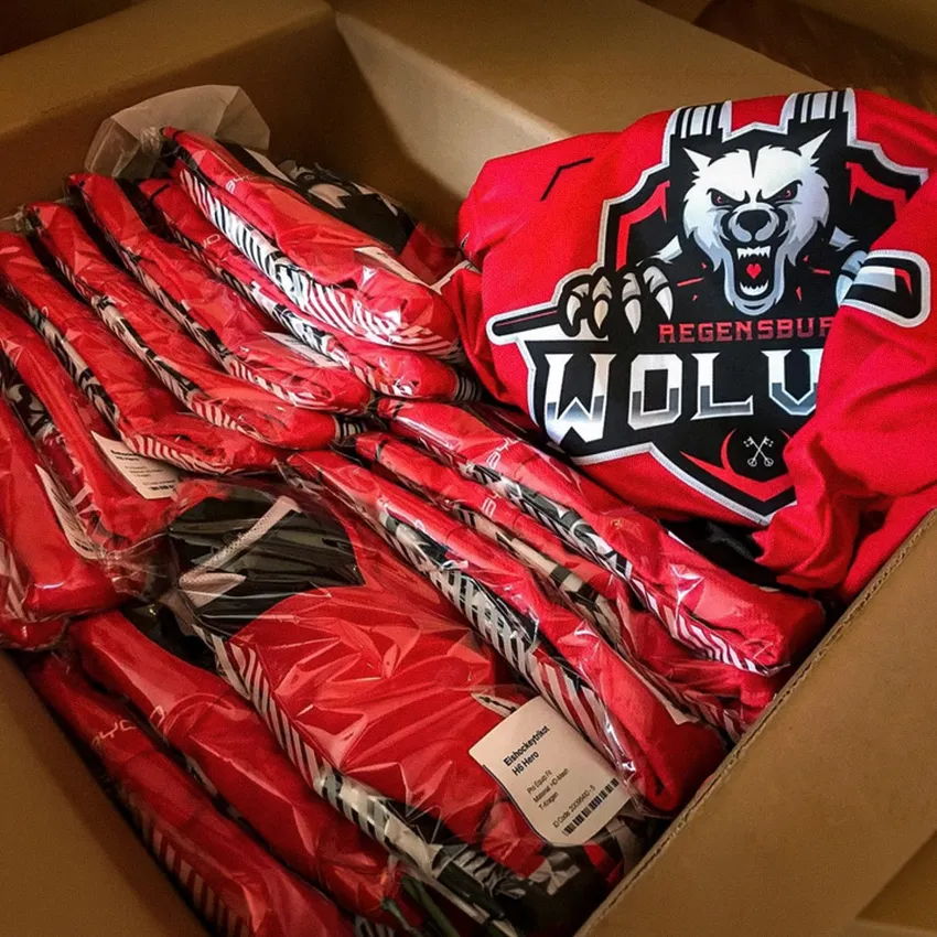 Een doos vol rode sportkleding met een wolf-logo en verschillende kledingstukken verpakt in doorzichtige folie.