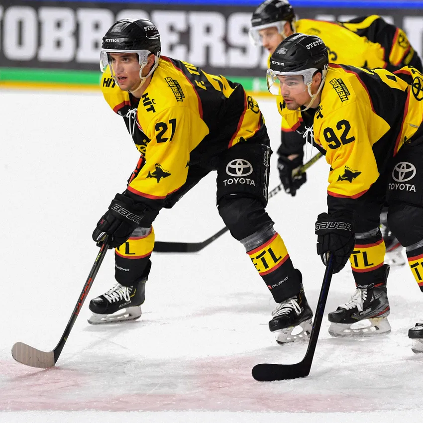Twee ijshockeyspelers in geel-zwarte shirts staan op het ijs en bereiden zich voor op de wedstrijd.