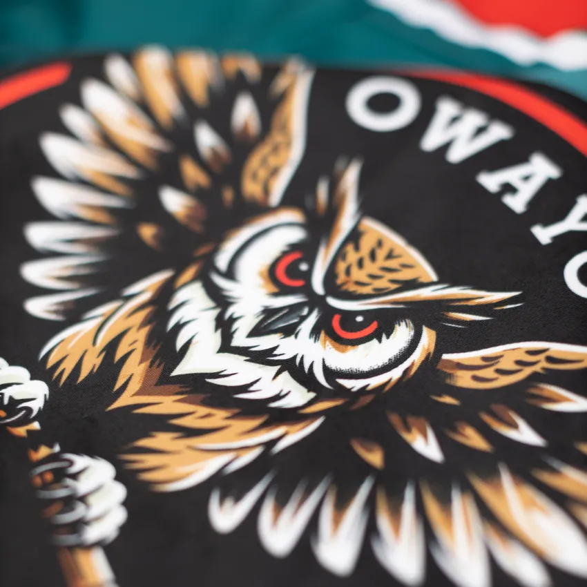 Een gedetailleerd, kleurrijk ontwerp van een uilenmotief op een zwarte achtergrond, te zien op een sportkledingstuk van owayo.