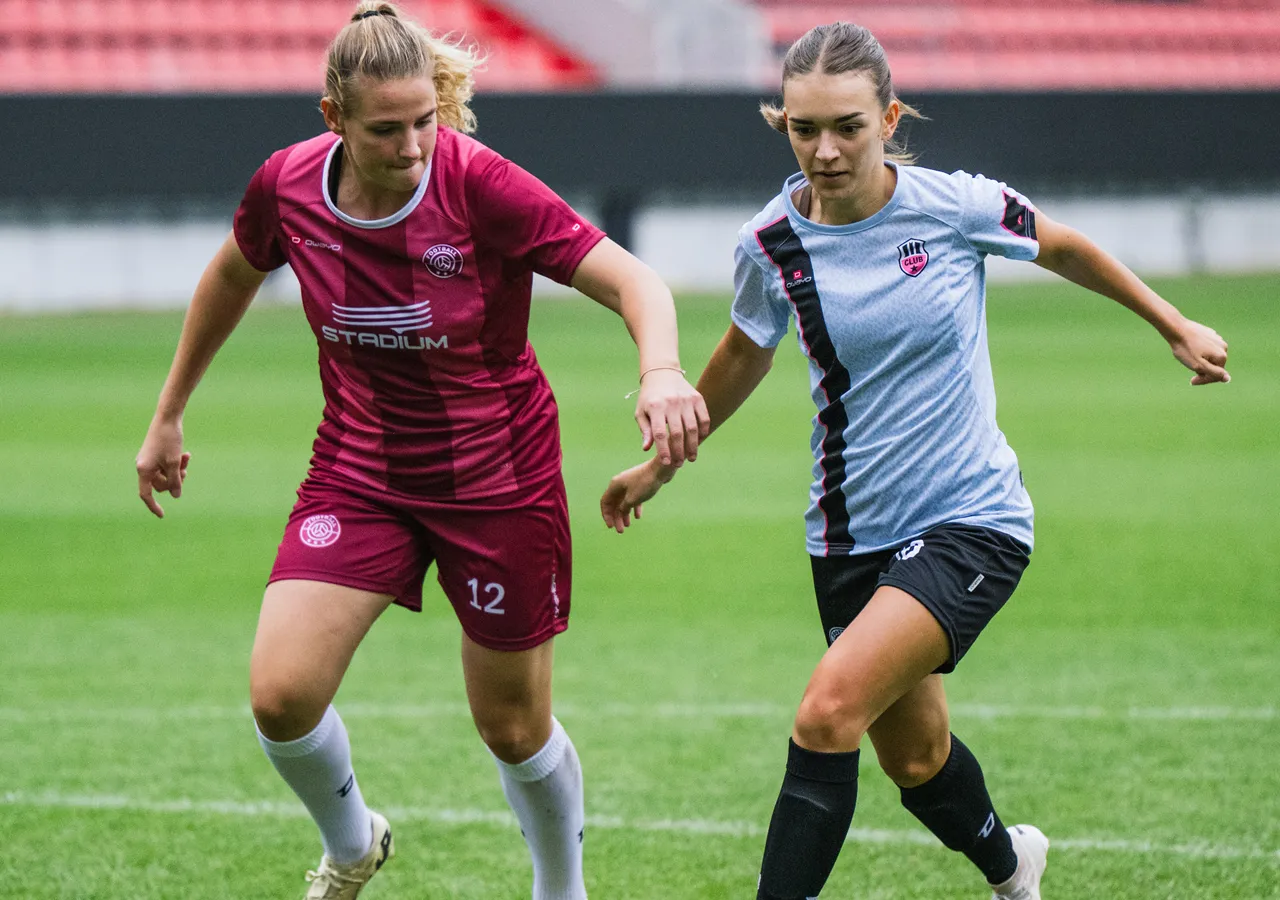 Twee vrouwelijke voetballers in kleurrijke shirts die met elkaar omgaan op een grasveld.