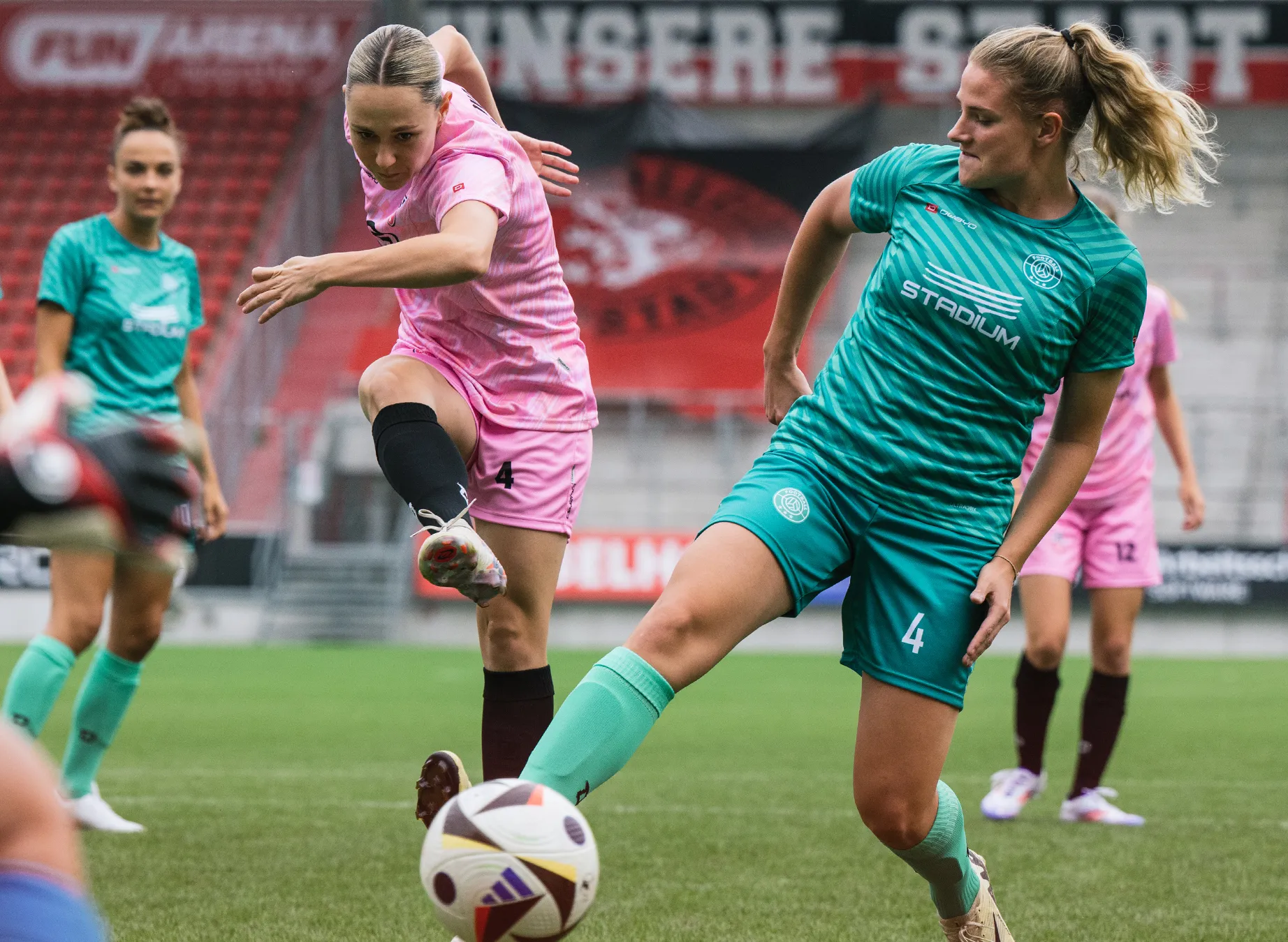 Twee vrouwen in kleurrijke sportshirts spelen voetbal op een grasveld.