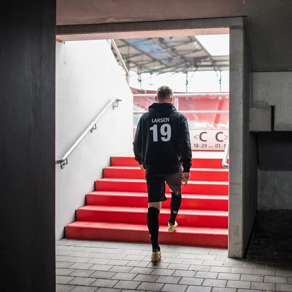 Een atleet in een zwarte hoodie en korte broek loopt een rode trap in een stadion op.