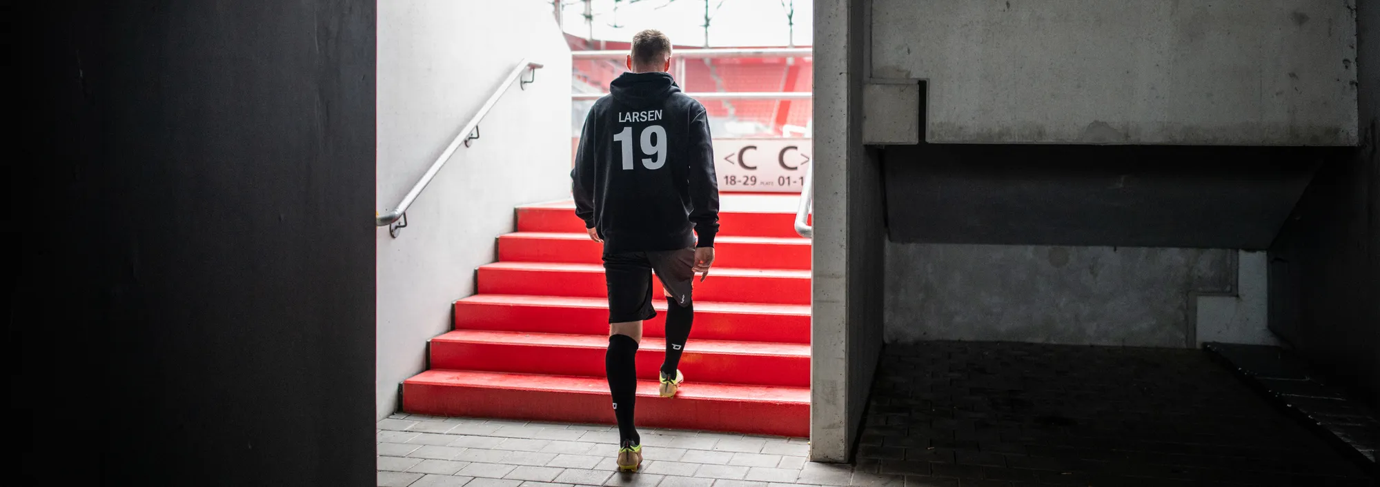 Een atleet loopt de trap af in sportkleding, op weg naar het veld.