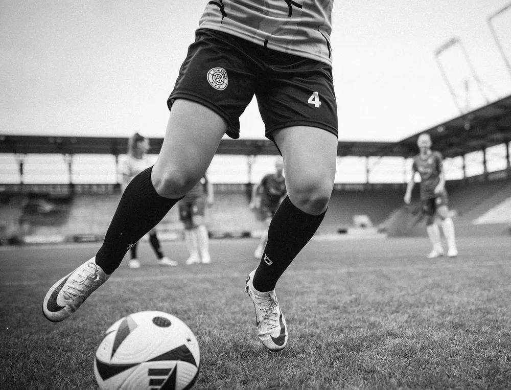 Een vrouwelijke voetballer in shorts en lange sokken die met een bal op het veld speelt.