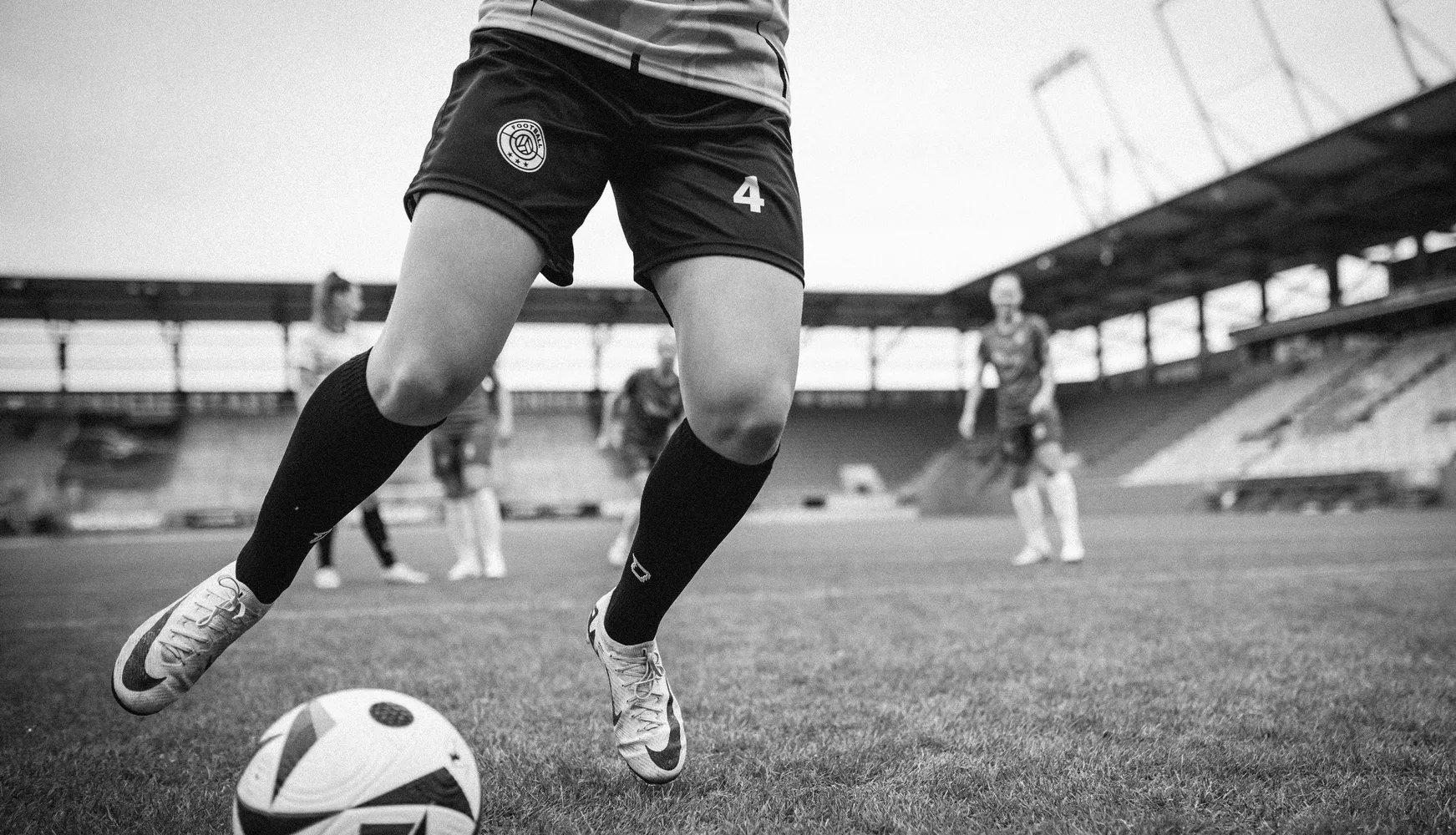 Een vrouwelijke speler in korte voetbalkorte broeken en lange sokken schopt een bal op een voetbalveld.