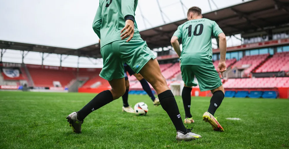 Twee voetballers in lichtgroene shirts en zwarte sokken trainen op een grasveld in een stadion.