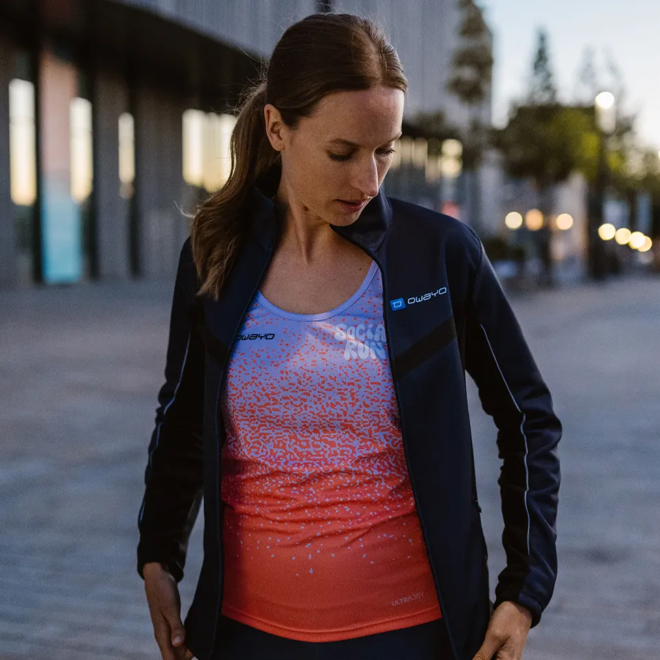 Een vrouw draagt een sportieve jas en een kleurrijke mouwloze top met een modern ontwerp terwijl ze op een stedelijke straat staat.