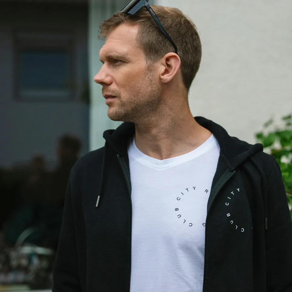 Een man draagt een zwarte hoodie over een wit T-shirt met een cirkelvormige print.