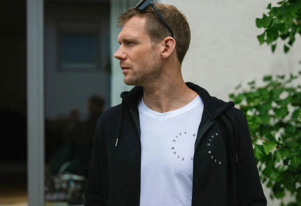 Een man staat zijwaarts met een zwarte hoodie en een wit T-shirt met een cirkelvormige print.