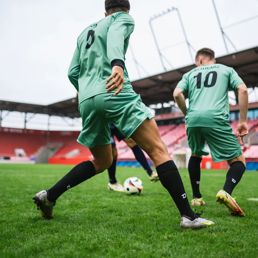Twee voetballers in groene shirts en zwarte sokken die op een grasveld met een bal spelen.
