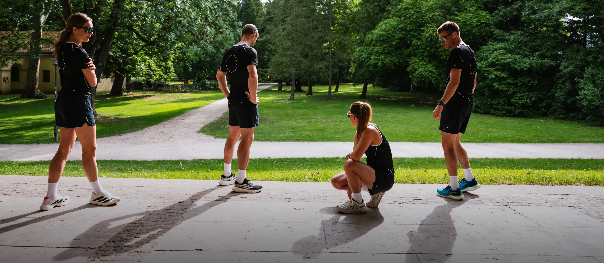Vier personen in sportkleding staan en zitten in een groene parklandschap.