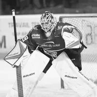 Een ijshockeyspeler in volledige uitrusting, inclusief helm, beschermingsmasker, handschoenen en beenbeschermers, staat in een verdedigende houding op het ijs.