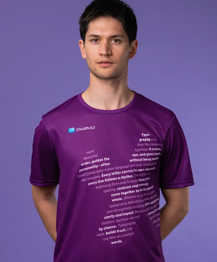Een man draagt een paarse sportshirt met typografische tekst op de voorkant, tegen een paarse achtergrond.
