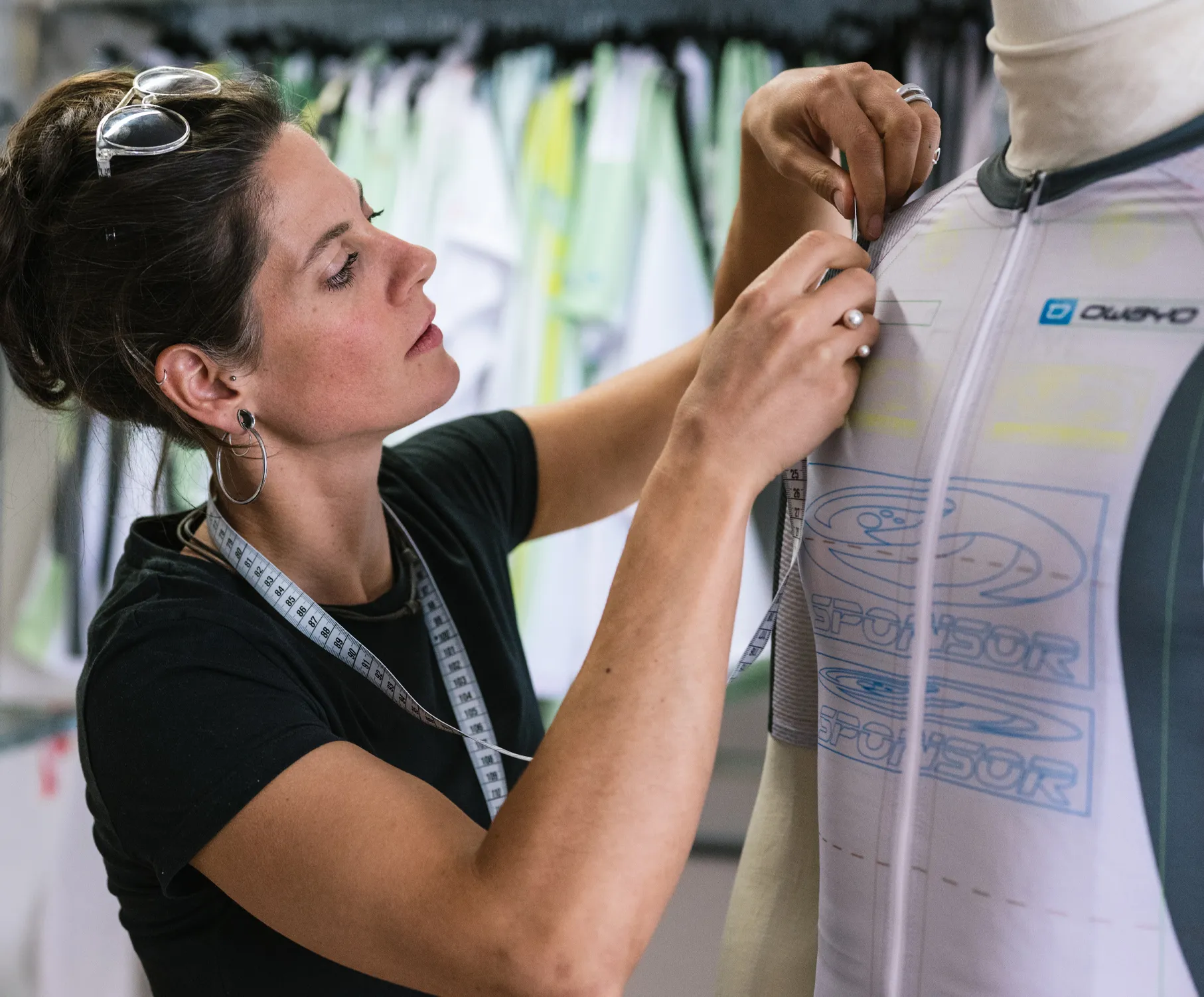 Een vrouw past een aangepast sportshirt aan op een mannequin, terwijl ze een meetlint om haar nek draagt.