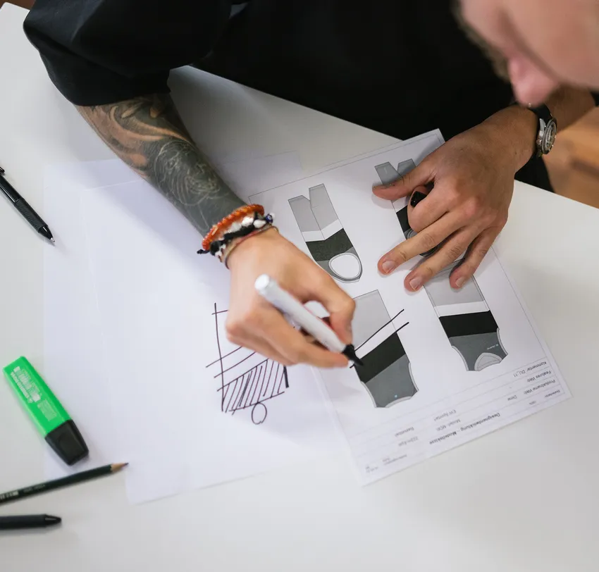 Een persoon met een tatoeage op de arm tekent met een marker op een vel papier ontwerpen voor aangepaste sportkleding.