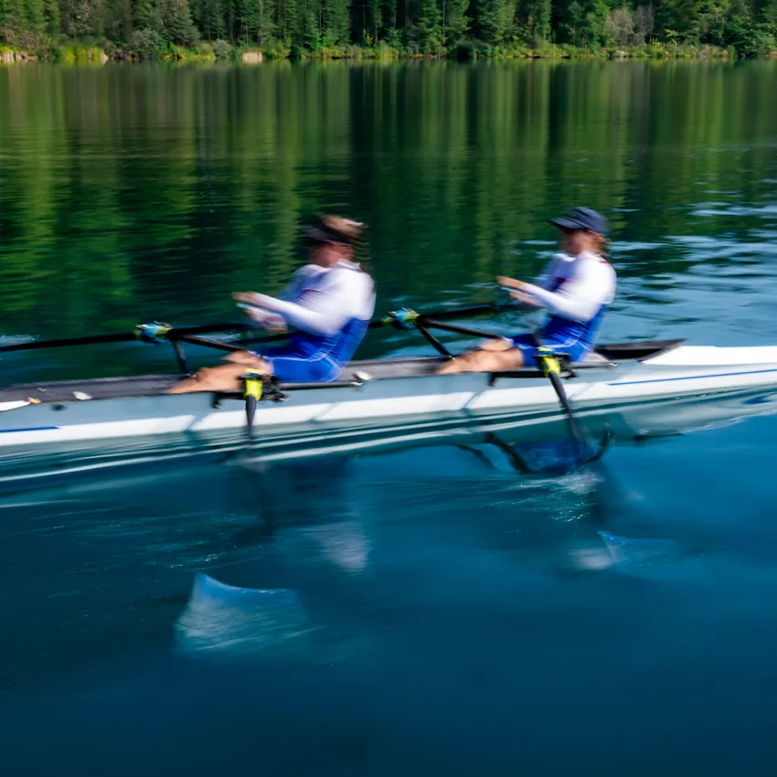 Twee roeiers in blauwe sportkleding die krachtige slagen maken op een kalme meer.