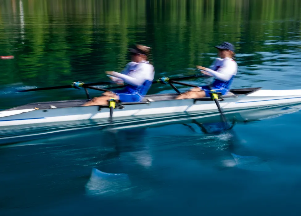 Twee roeiers in blauwe sportkleding roeien synchroon op kalm water.